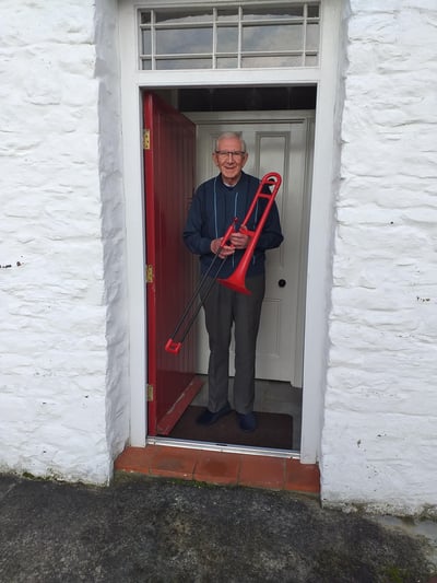 Adult trombone learner George pictured in a doorway with a red pBone.